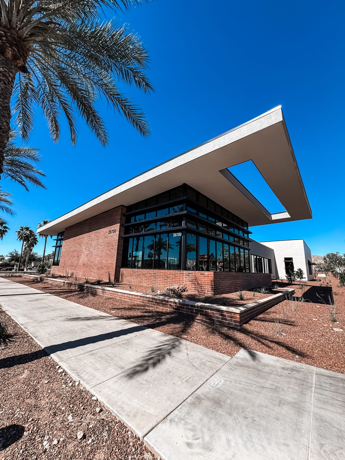 Brick and glass office building numbered 20700, with palm trees along the sidewalk